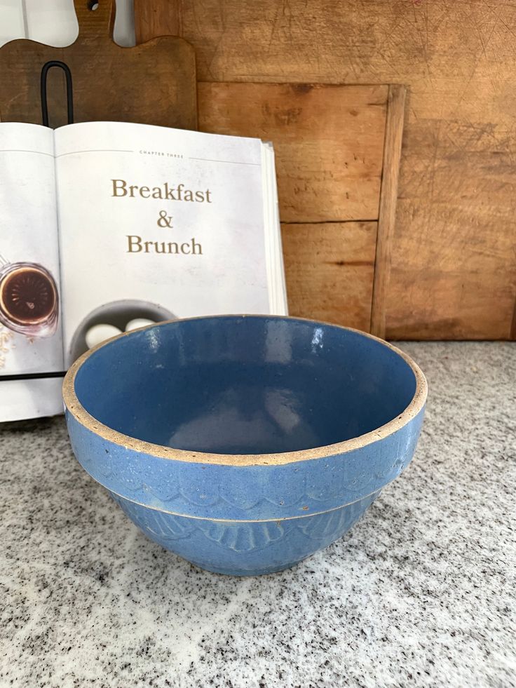 a blue bowl sitting on top of a counter next to an open book