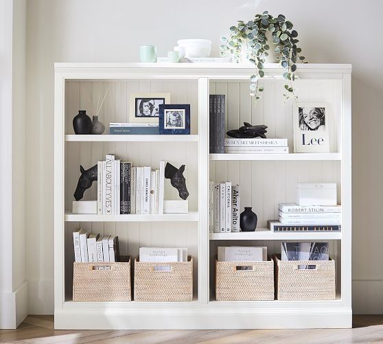 a white bookcase with books and baskets on it