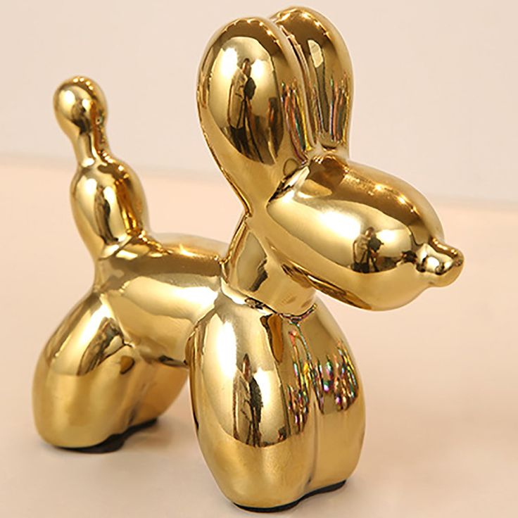 a shiny gold dog statue sitting on top of a table next to a white wall