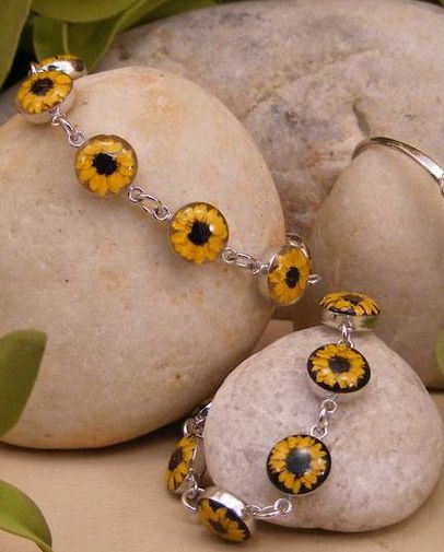 two yellow and black flowers are attached to a silver bracelet on top of a rock