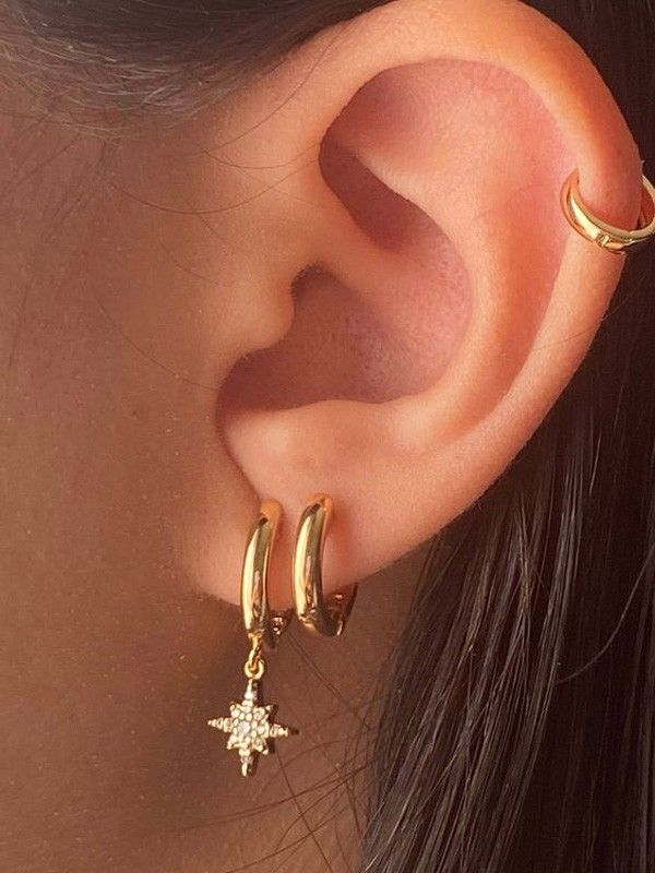 a close up of a person's ear wearing gold hoops and star earrings