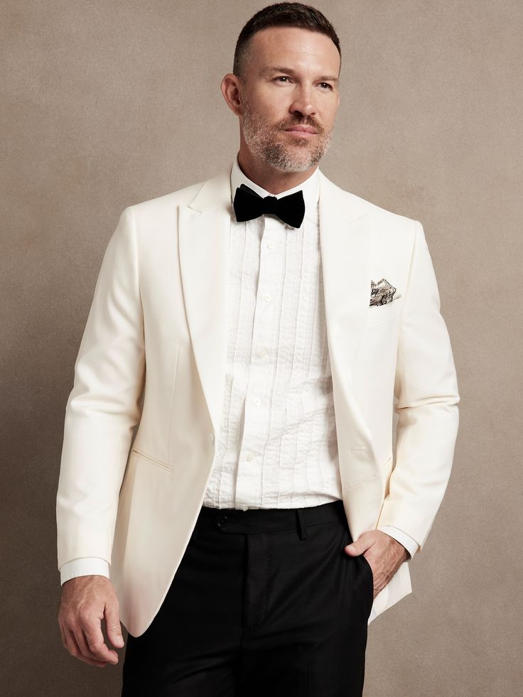 a man in a white tuxedo and bow tie poses for a photo with his hands in his pockets