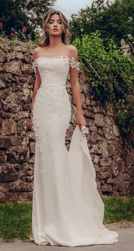 a woman in a white wedding dress standing on the side of a road wearing an off shoulder gown