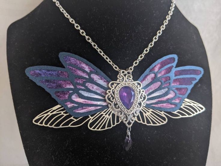 This gorgeous necklace features purple, black, and silver fairy wings with a opalescent purple gem in the middle. A drop crystal hangs from the center. Perfect for special occasions or to add a bit of magic to your everyday! Faerie Wedding, Witch Crystals, Goblin Market, Magical Aesthetic, The Red Shoes, Purple Fairy, Fantasy Witch, Aesthetic Fairy, Magical Accessories