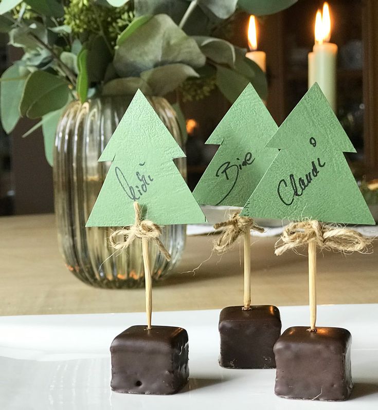 three pieces of chocolate are sitting on a plate with small trees in front of them