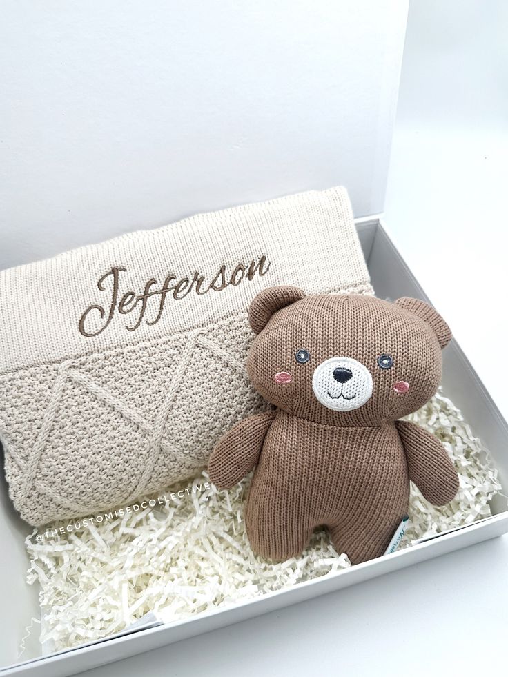 a brown teddy bear sitting next to a white pillow in a box with the name jefferson on it