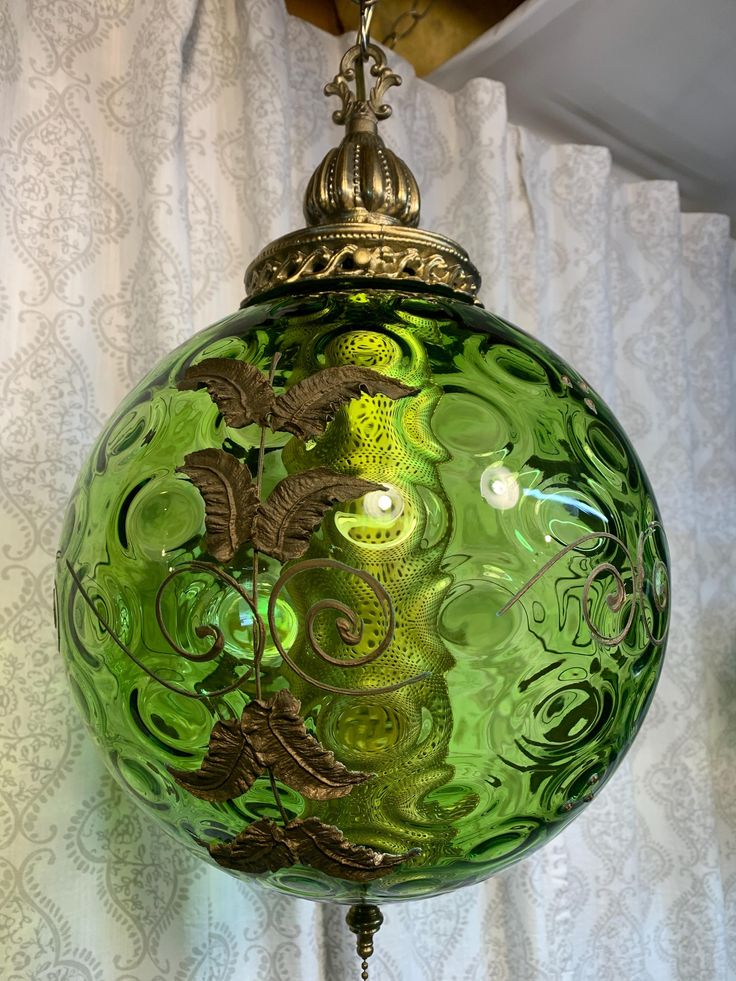 a green glass ornament hanging on a curtain rod with an intricate design in the center