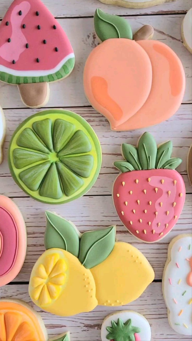 some decorated cookies are sitting on a white wooden table and one has a slice of fruit