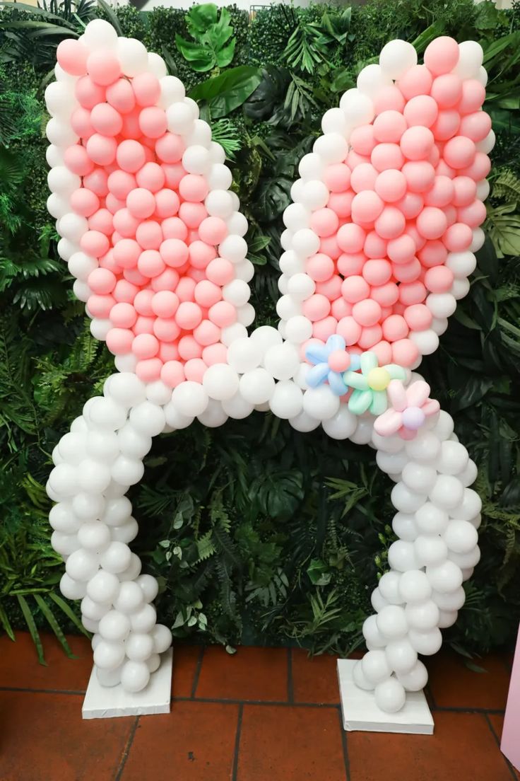 an animal made out of balloons sitting on top of a brick floor next to a green wall