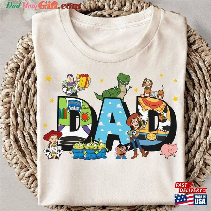 a t - shirt with the word dad written in cartoon characters on it, sitting next to a wicker basket