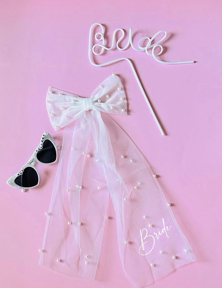 a white bow, sunglasses and bride sign on a pink background with the word bride spelled out