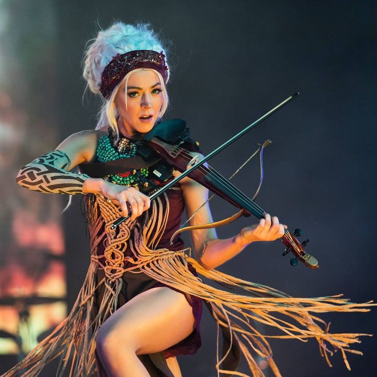 a woman with white hair holding a violin and wearing an elaborate outfit while performing on stage