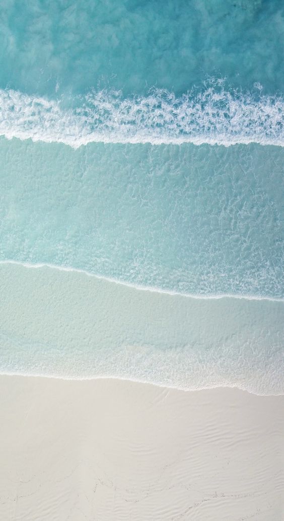 an aerial view of the ocean and beach with two people walking in the sand near the water