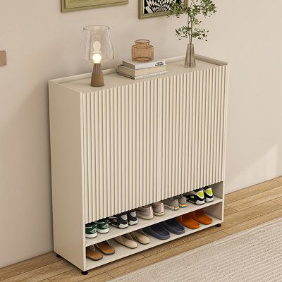 a white cabinet with shoes on it next to a rug and pictures hanging on the wall