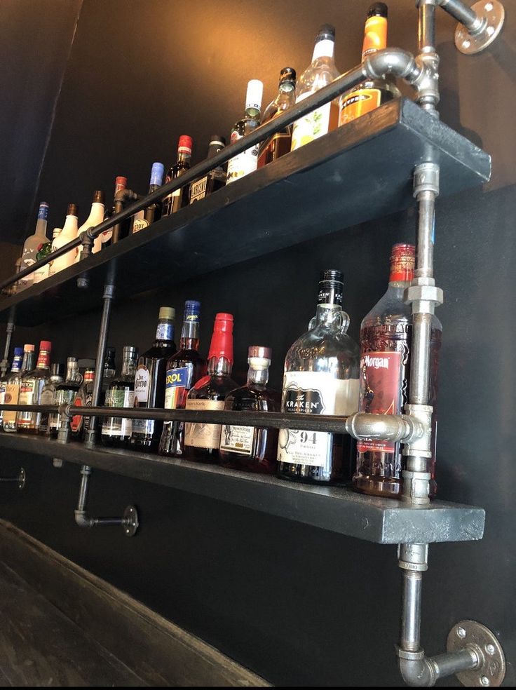 bottles are lined up on the shelf behind the faucet in this liquor bar