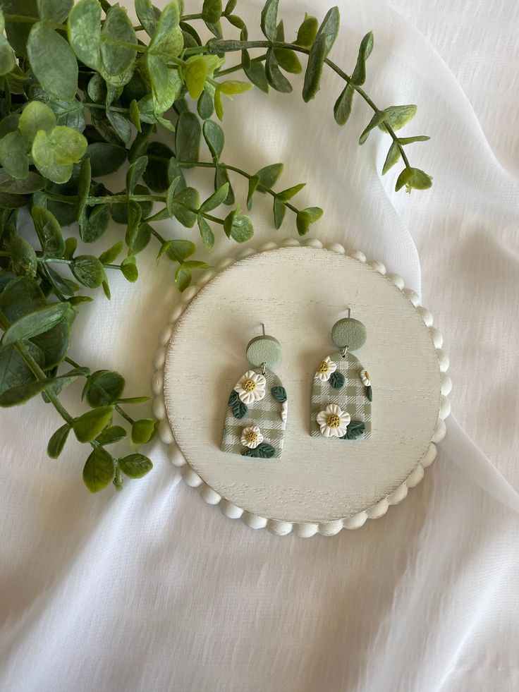 a pair of earrings sitting on top of a white plate next to a green plant