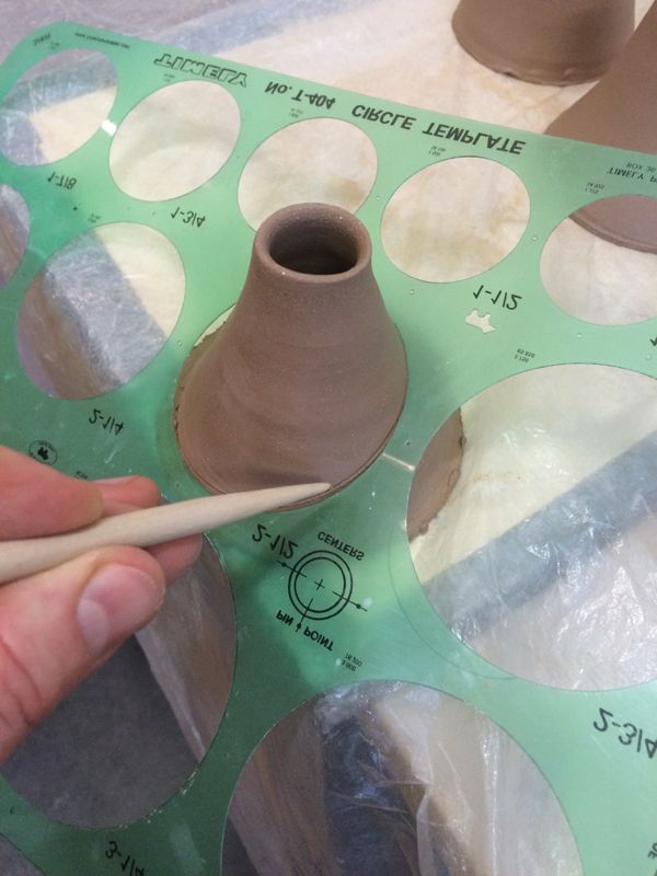 a person holding a pair of scissors next to a clay vase on top of a table