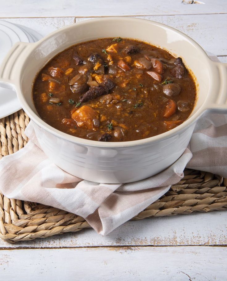 a white bowl filled with soup on top of a wicker place mat next to a spoon