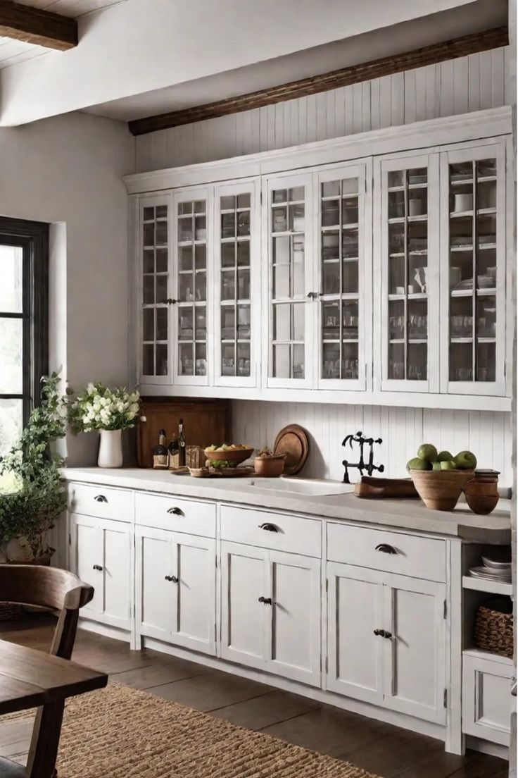 a large kitchen with white cabinets and wooden table in front of windows, potted plants on the counter