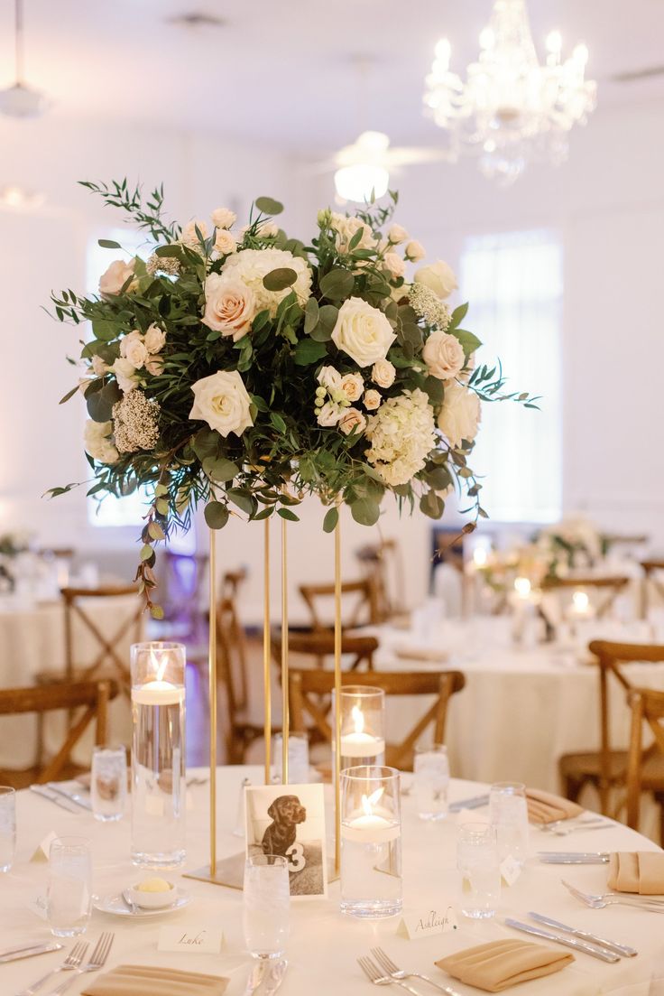 a centerpiece with flowers and greenery on a table in a banquet or wedding reception