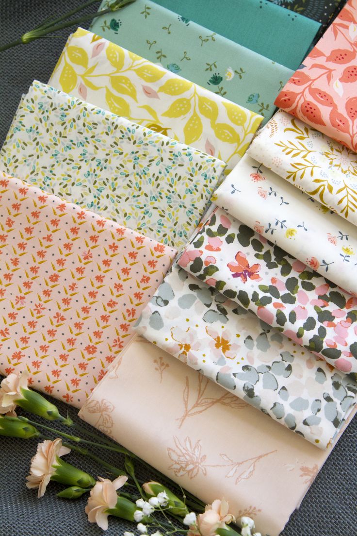 a bunch of different types of fabric sitting on top of each other next to flowers