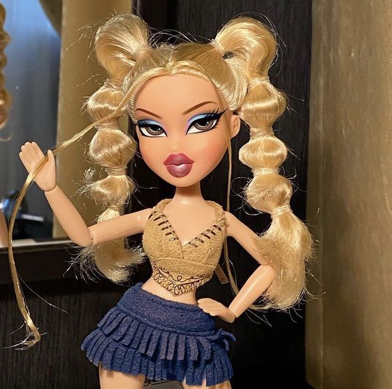 a close up of a doll with blonde hair wearing a skirt and holding a wand