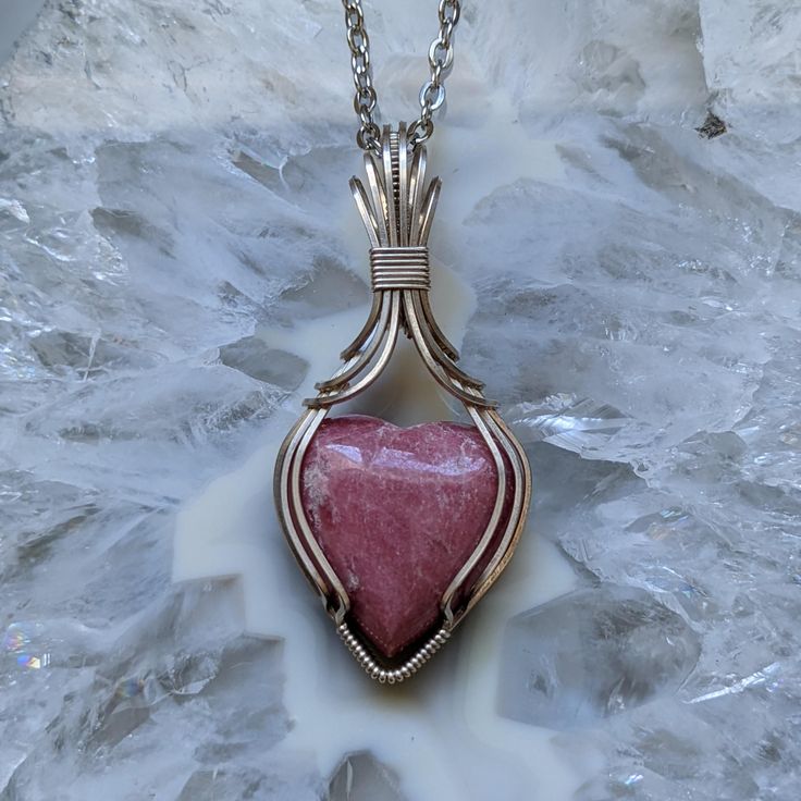 This pretty rhodonite heart has been hand wrapped in sterling silver wire with an Art Deco inspired bail and comes with an 18" clasped silver colored* chain, gift packaging and free tracked shipping in North America.  *Please note the complimentary chain is NOT sterling silver* Rhodonite Heart and Sterling Silver Wire Wrapped Pendant Necklace Handmade Heart Pendant Jewelry For Healing, Hand Wrapped Heart Pendant Jewelry Gift, Valentine's Day Adjustable Wire Wrapped Jewelry, Wire Wrapped Heart Pendant Jewelry Gift, Heart-shaped Wire Wrapped Necklace For Gift, Heart-shaped Wire Wrapped Necklace Gift, Silver Wire Wrapped Necklace For Valentine's Day, Wire Wrapped Jewelry For Valentine's Day Gift, Sterling Silver Hand Wrapped Necklace For Gift