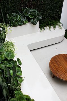 a wooden plate sitting on top of a white table next to green plants and shrubbery