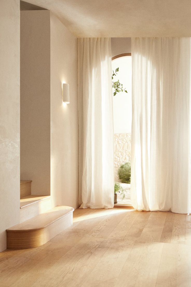 an empty room with wooden floors and white curtains on the windowsill, along with a potted plant