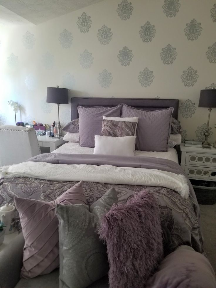 a bed with purple and white pillows in a bedroom next to a wallpapered wall