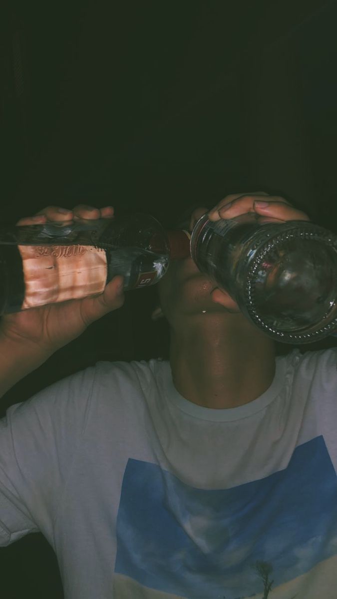 a man is drinking from a glass bottle