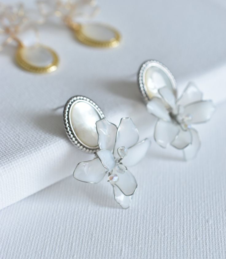 The luna earrings are a mesmerizing fusion of vintage charm and contemporary flair. The shimmering mother of pearl pendant is beautifully accentuated by a delicate dip art flower and moonlight pistil, creating a piece that is both timeless and on-trend. With their versatile aesthetic, these earrings seamlessly transition from day to night, effortlessly elevating any look. DETAILS ❁Hand crafted dip resin art flower with glossy finish. ❁Features an elegant design, highlighted by a stunning mother Delicate Silver Jewelry With Flower Decoration, Wedding Jewelry With Pearl Charm And Mother Of Pearl, Elegant Mother Of Pearl Jewelry In Pearl White, Delicate Pearl Charm Flower Earrings For Wedding, Silver Feminine Earrings With Pearl Charm, Feminine Pearl Earrings In Silver, Feminine Silver Earrings With Pearl Charm, Feminine Silver Pearl Earrings, Delicate Mother Of Pearl Jewelry For Wedding