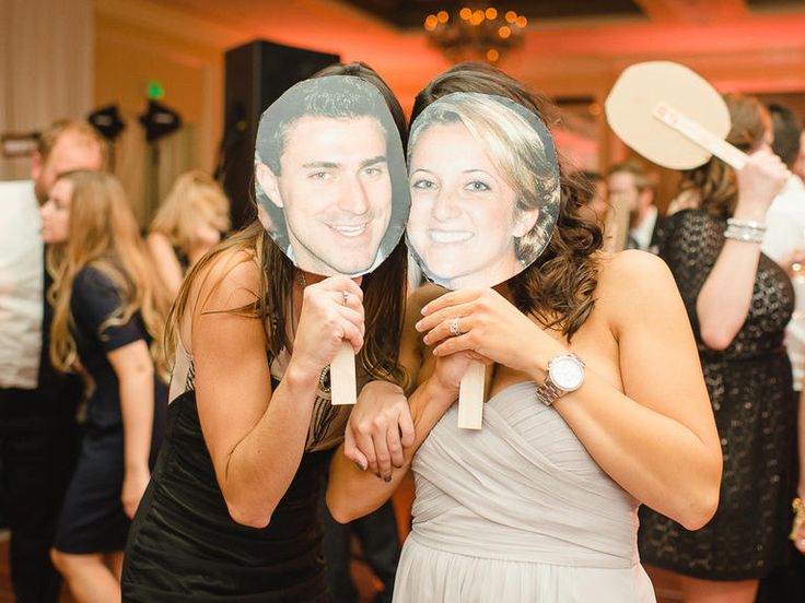 two people holding up masks in front of their faces at a party with other people on the dance floor