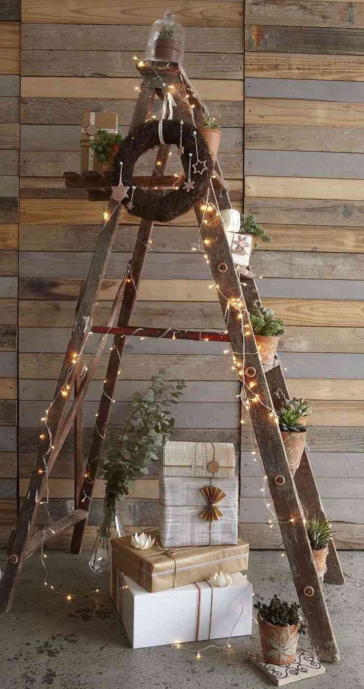 a christmas tree made out of wooden ladders with lights and presents under it in front of a wood wall