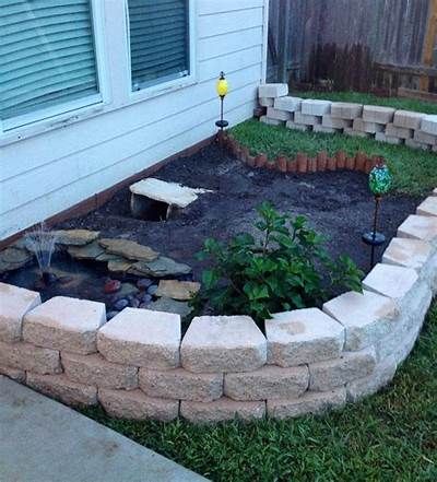 a small garden area with rocks and plants in it, along side a house on the grass