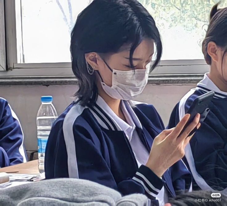 two girls wearing face masks looking at their cell phones