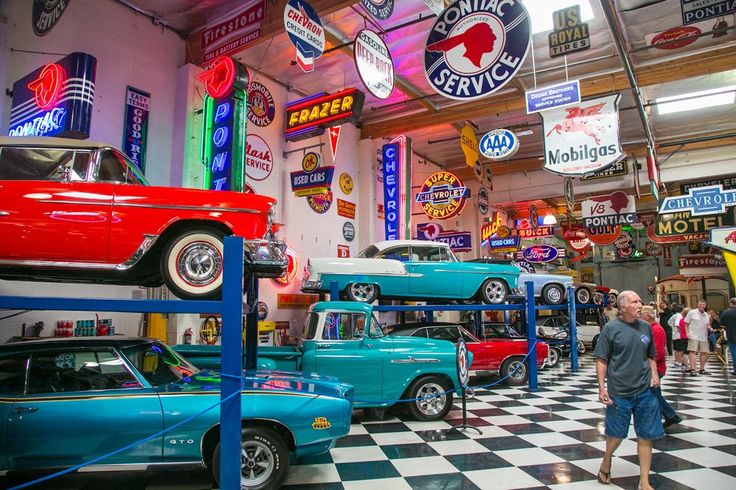 several classic cars are on display in an auto shop with neon signs and advertisements above them