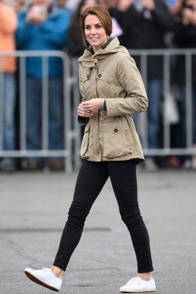 a woman walking down the street in black pants and a tan jacket with white shoes