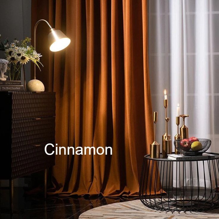 a table with some fruit on it in front of a curtained window and a lamp