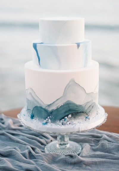 a three tiered cake with blue and white frosting sitting on top of a table