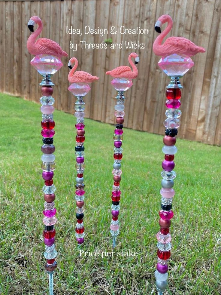 three pink flamingos sitting on top of glass candlesticks in front of a fence