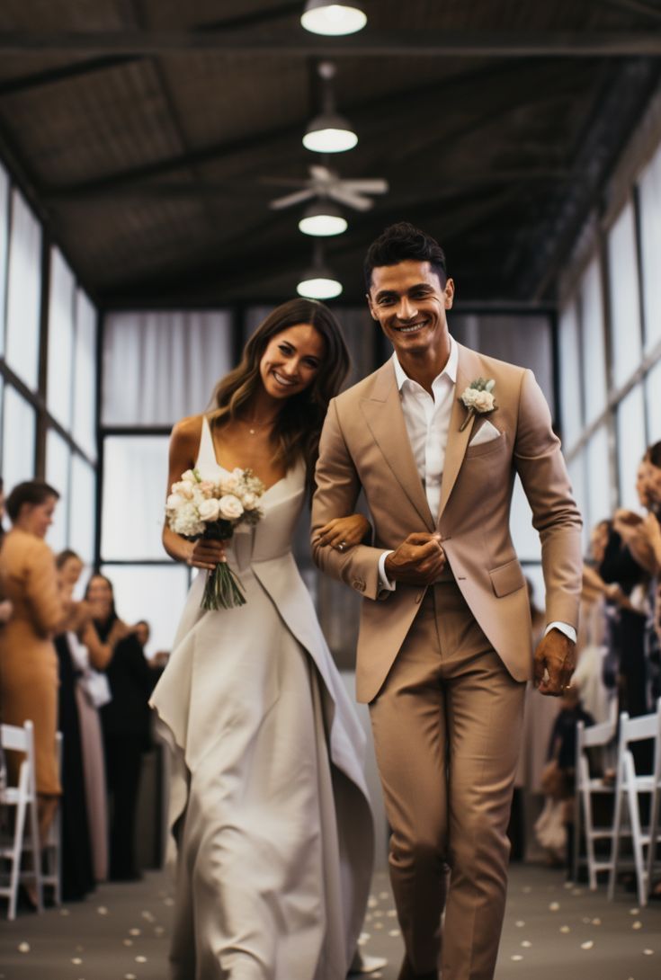 A bride and groom, hand in hand, walking down the aisle, their wedding attire radiating in dark beige and white. The scene captures the essence of pop inspo and the beauty of ready-made artistry, marking a moment of pure love and commitment. Beige And White Outfit Men, Groom Attire Tan, Old Money Groom Suit, Light Brown Groomsmen Suits, Beige Suit Wedding, Groom Suit Bow Tie, Beige Groom Suit, Beige Wedding Suit, Brown Groomsmen Suits