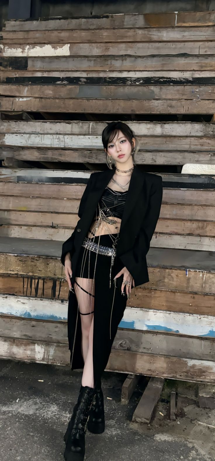 a woman is sitting on some wooden steps wearing black boots and a skirt with chains around her waist