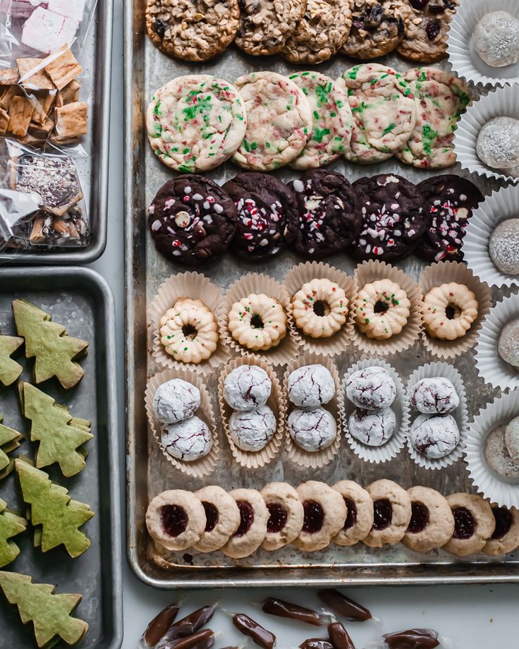 an assortment of cookies and pastries in trays next to christmas tree shaped cookies