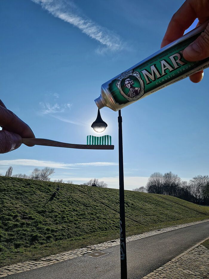 someone is holding a toothbrush next to a tube of toothpaste on a pole