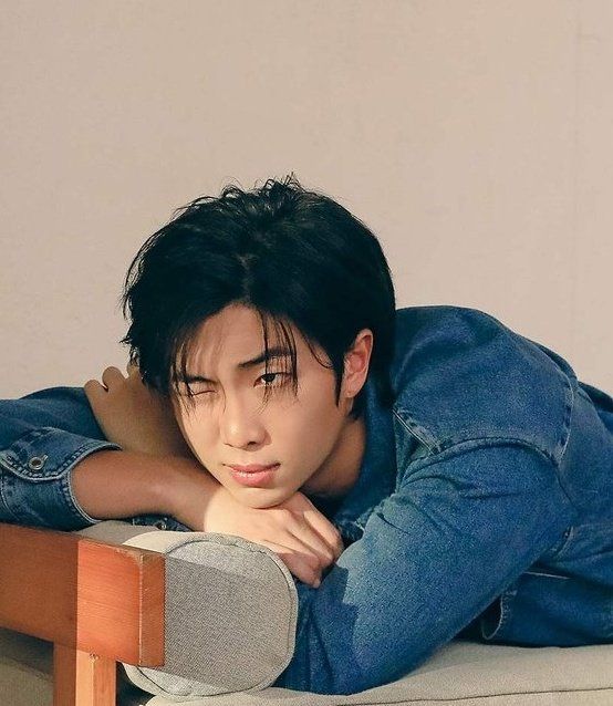 a young man laying on top of a bed next to a wooden frame with his arms crossed