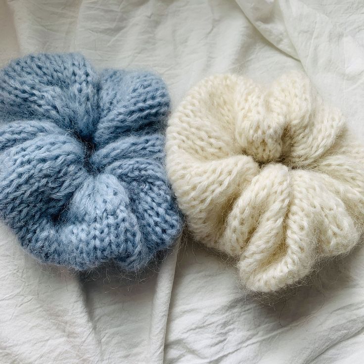 two knitted scrunffs laying on top of a white bed sheet, one blue and the other beige