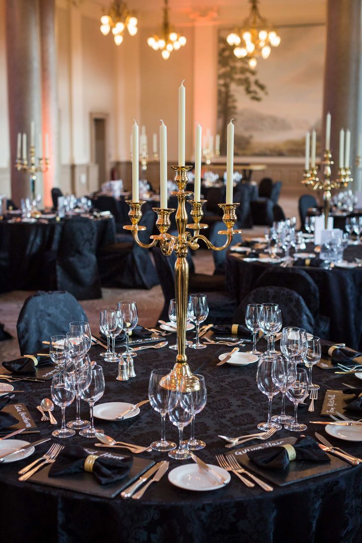 a table set up with black linens and gold place settings for an elegant dinner