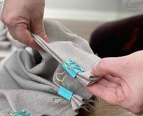 someone is sewing something on top of a bag with blue ribbon and gold hardware, while another person's hands are holding the fabric