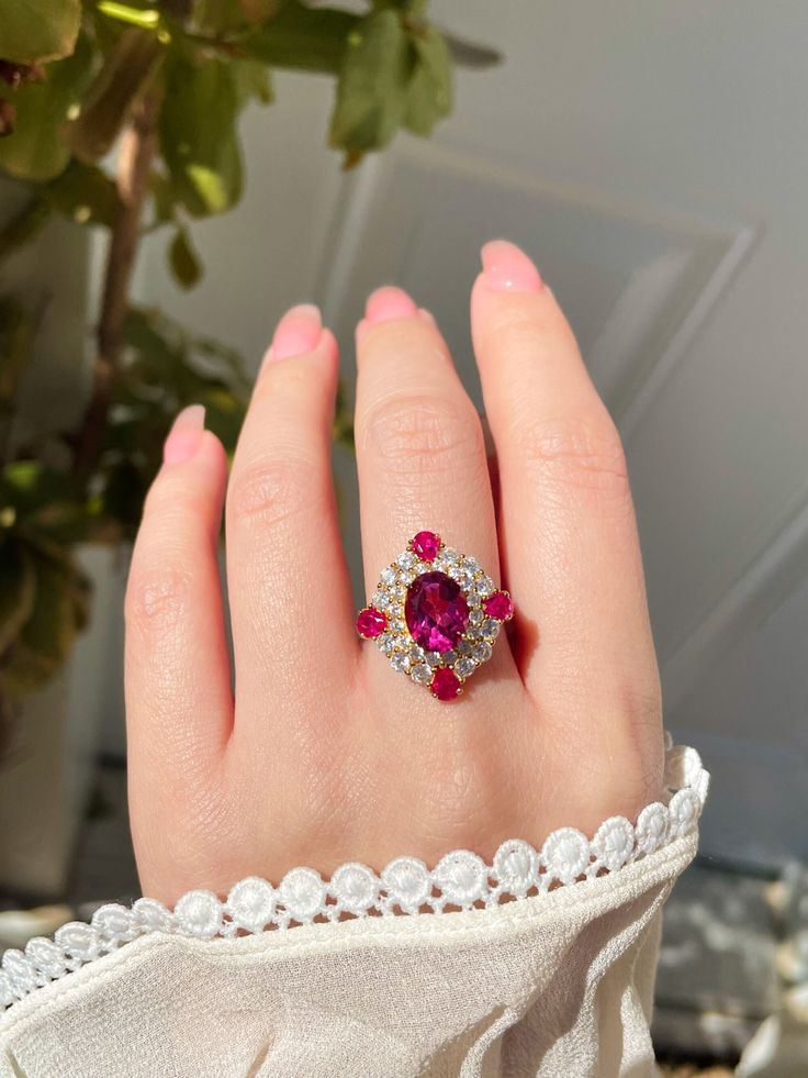 Description:  This ring features a vibrant oval-cut pink topaz in the center, haloed by four small pear-cut pink topaz and multiple sparkling brilliant-cut cubic zirconia stones. The color of this natural pink topaz comes in shades of soft pink and fiery red. As a symbol of love and affection, pink topaz can bring good fortune in love, and provide happiness and vitality to any relationship. It is a great gift for your loved ones and of course a treat for yourself. Pamper yourself and your loved ones! Details: - Stone Name: Pink Topaz - Birthstone: November - Main Stone Shape: Oval - Main Stone Size: 7*9 mm - Metal: Yellow Gold Vermeil / White Gold Vermeil - Due to the nature of gemstones, each piece may slightly vary in color and contain natural inclusions. Also, the color and the halo may Oval Ruby Ring For Party, Oval Ruby Ring For Parties, Elegant Pear-shaped Pink Ruby Ring, Elegant Pink Pear-shaped Ruby Ring, Pink Cluster Ring With Gemstone, Pink Cluster Gemstone Ring, Pink Oval Cluster Ring Fine Jewelry, Pink Marquise Rings With Center Stone, Pink Oval Ruby Ring With Center Stone